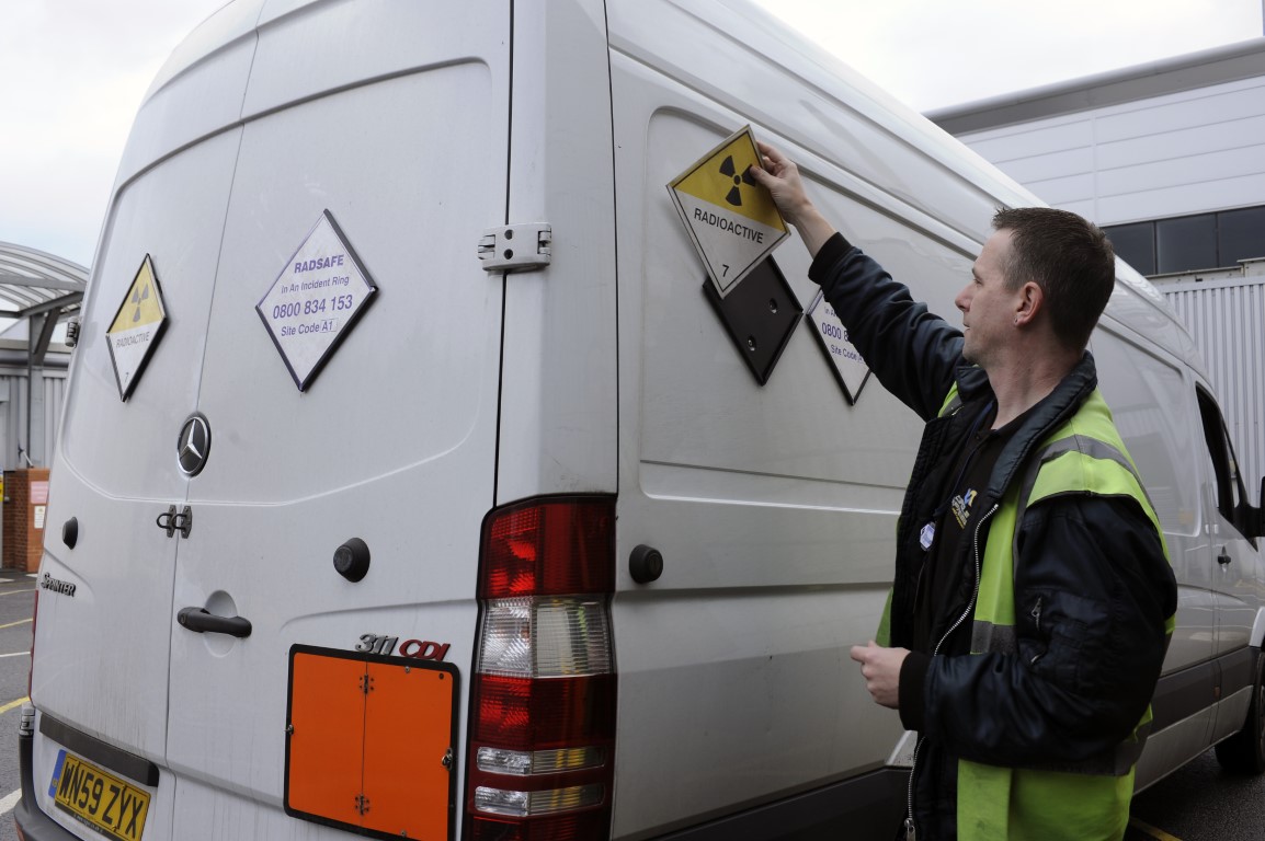 Rys. Pojazdy przewożące materiały promieniotwórcze powinny być oznakowane nalepką ostrzegawczą z charakterystyczną czarną „koniczynką”. Umieszczona na nalepce cyfra jest międzynarodowym oznaczeniem materiałów promieniotwórczych przyjętym przez ONZ. Na pojeździe powinien znajdować się również znak ostrzegawczy w postaci prostokątnej pomarańczowej tablicy. Podczas transportu niektórych materiałów promieniotwórczych na tablicy tej będą umieszczone liczby określające numer rozpoznawczy materiału i numer rozpoznawczy zagrożenia wg klasyfikacji ONZ. Źródło: IAEA